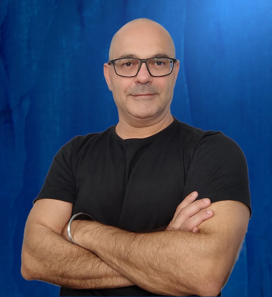 Elio Haddad, coach executivo, sorrindo de braços cruzados diante de um fundo azul