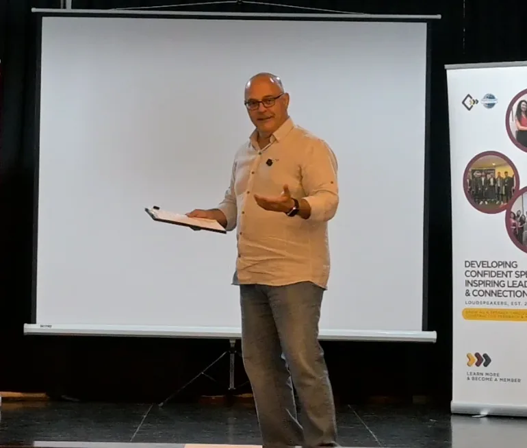 Elio Haddad leading a communication session in front of a screen and club banners in Lebanon